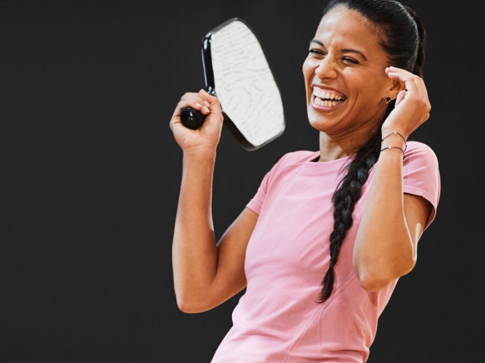 a woman smiles and laughs while holding a pickleball paddle