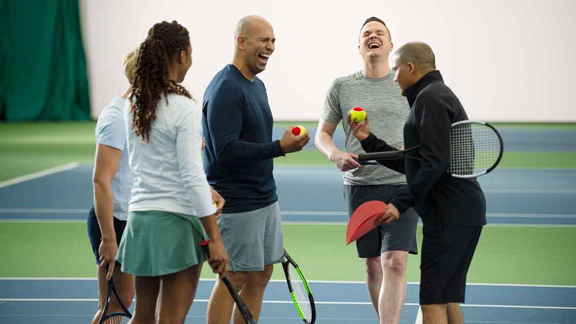 a group of adults enjoy a tennis lesson on an outdoor court