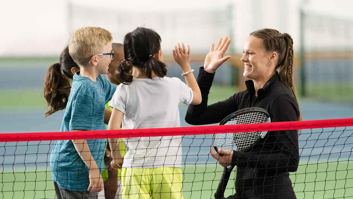 a group of kids give their tennis instructor a high five