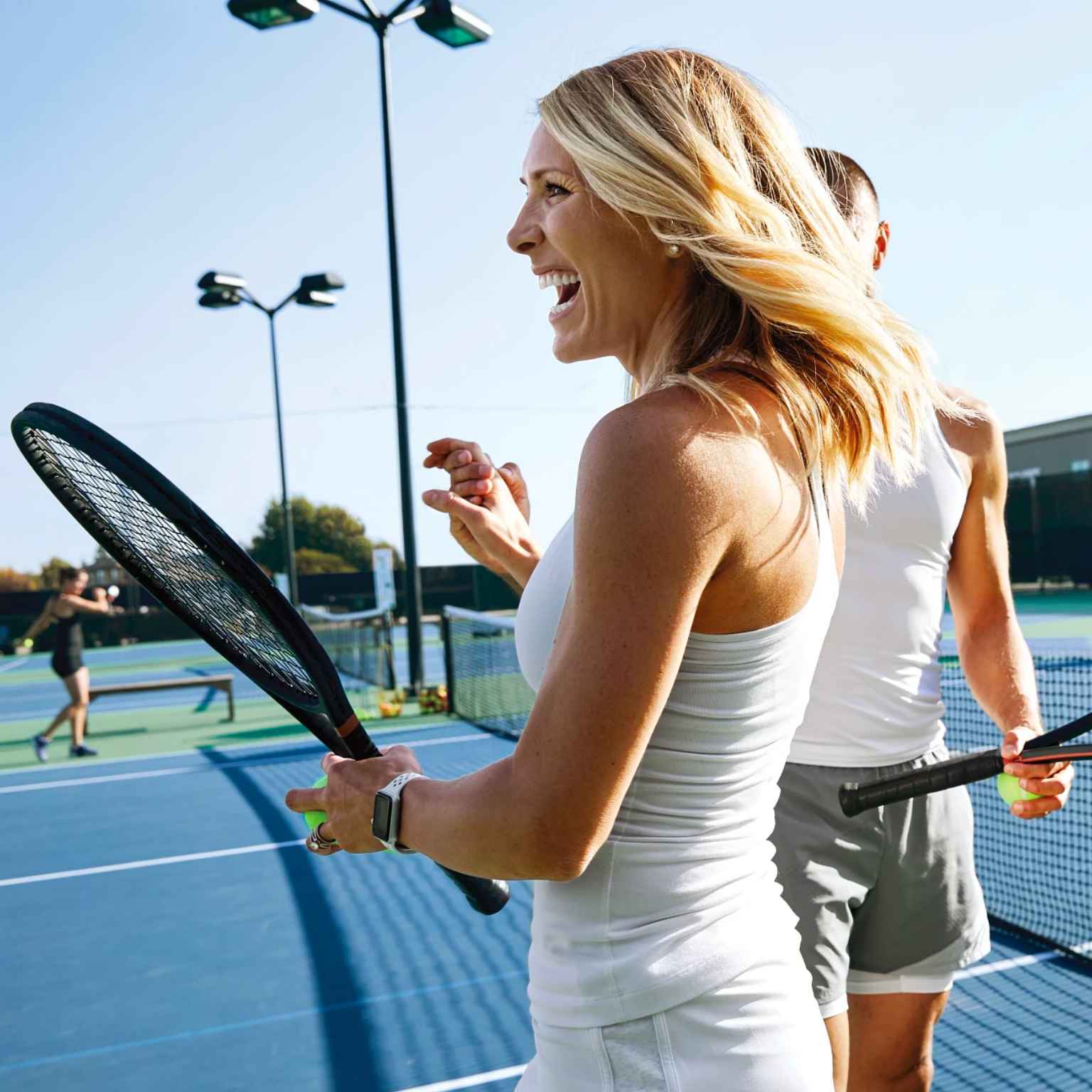 Two women smiling playing tennis on an outdoor court