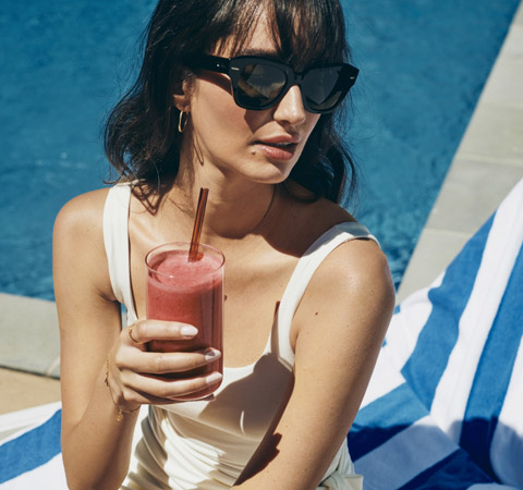 woman in sunglasses drinking a red smoothie