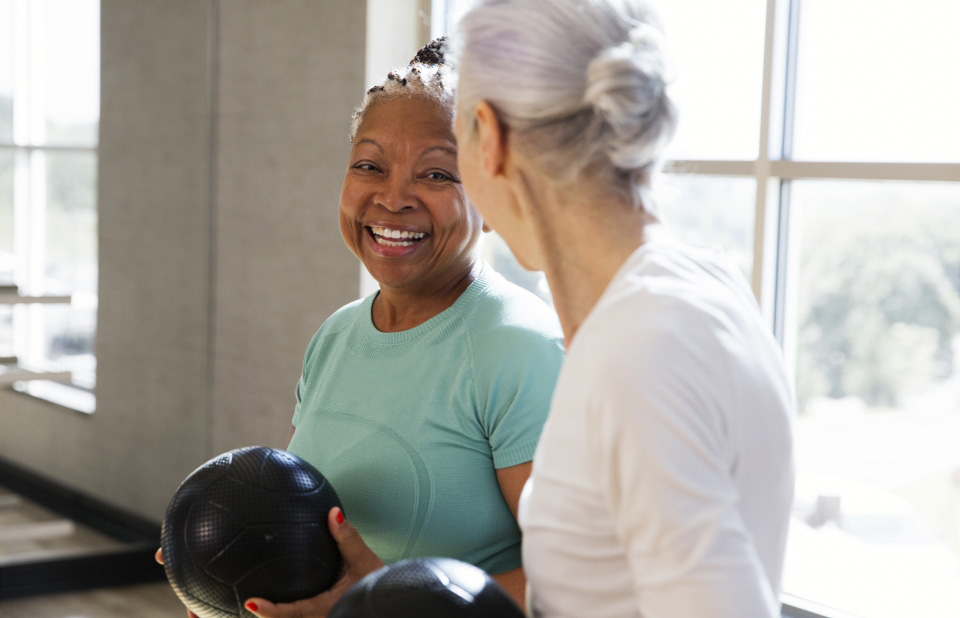 2 women share a smile while holding medicine balls