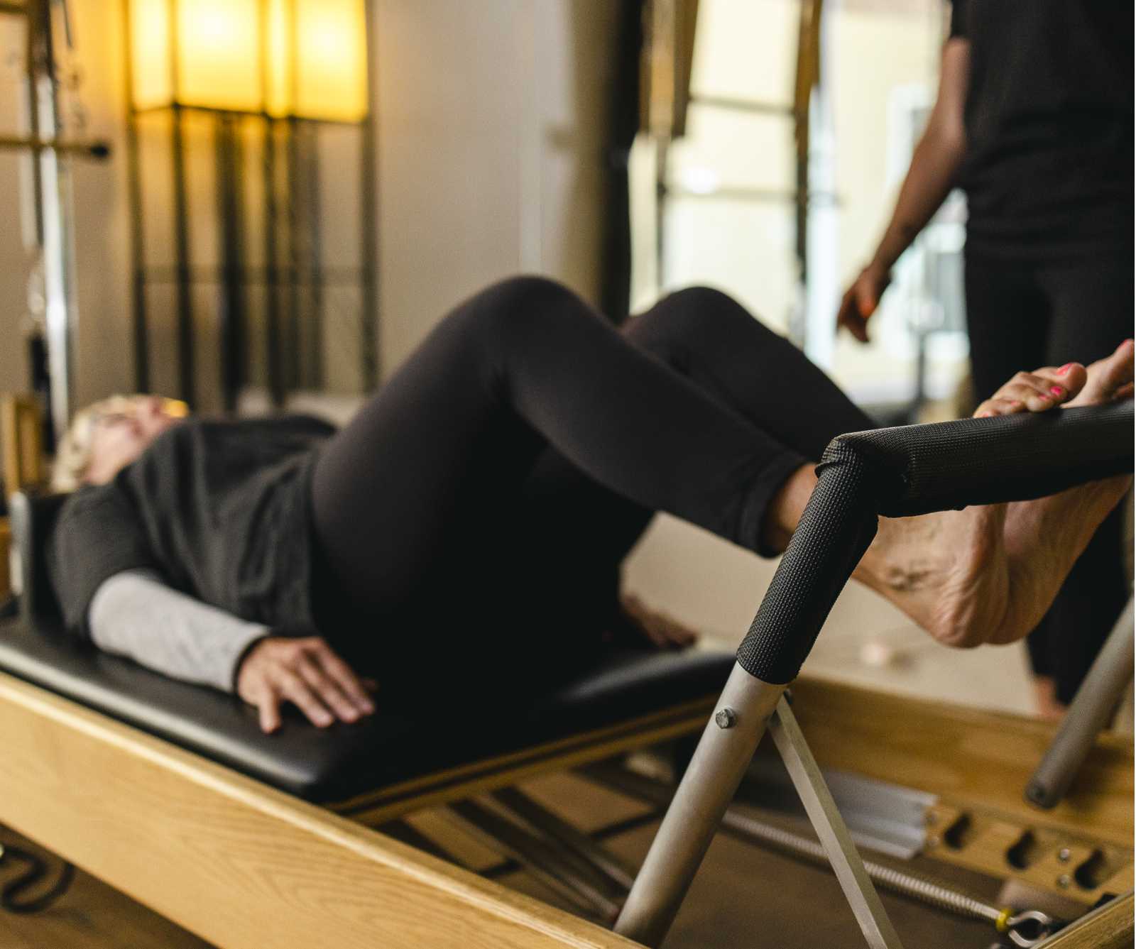A woman uses her legs to push on the pilates reformer bar