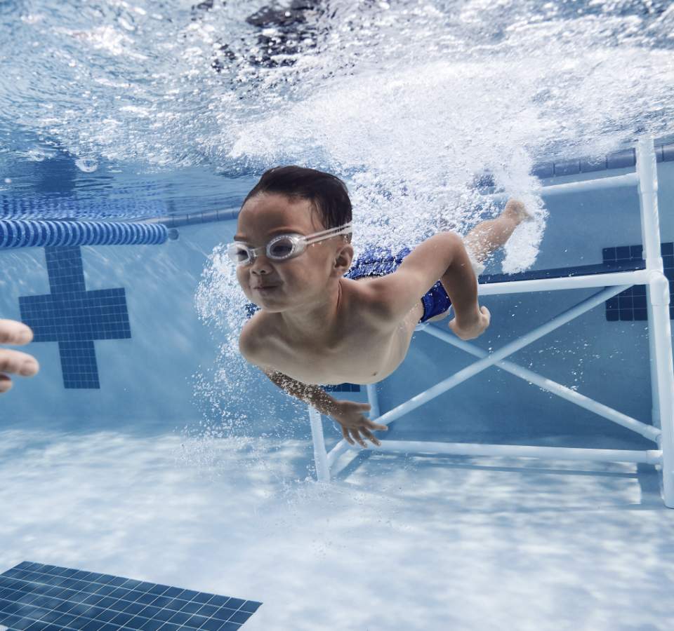 a young boy swims underwater toward outstretched hands