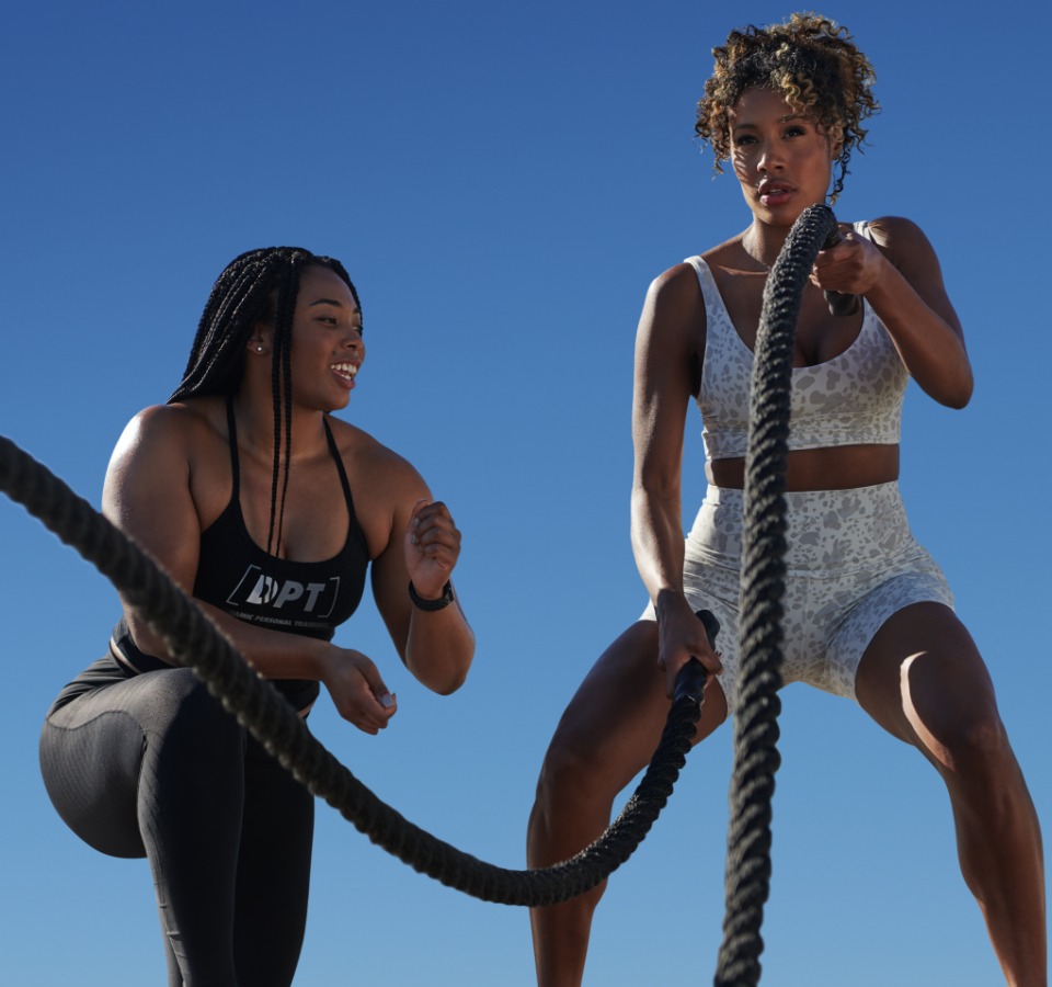 a trainer coaches a woman while she swings battle ropes