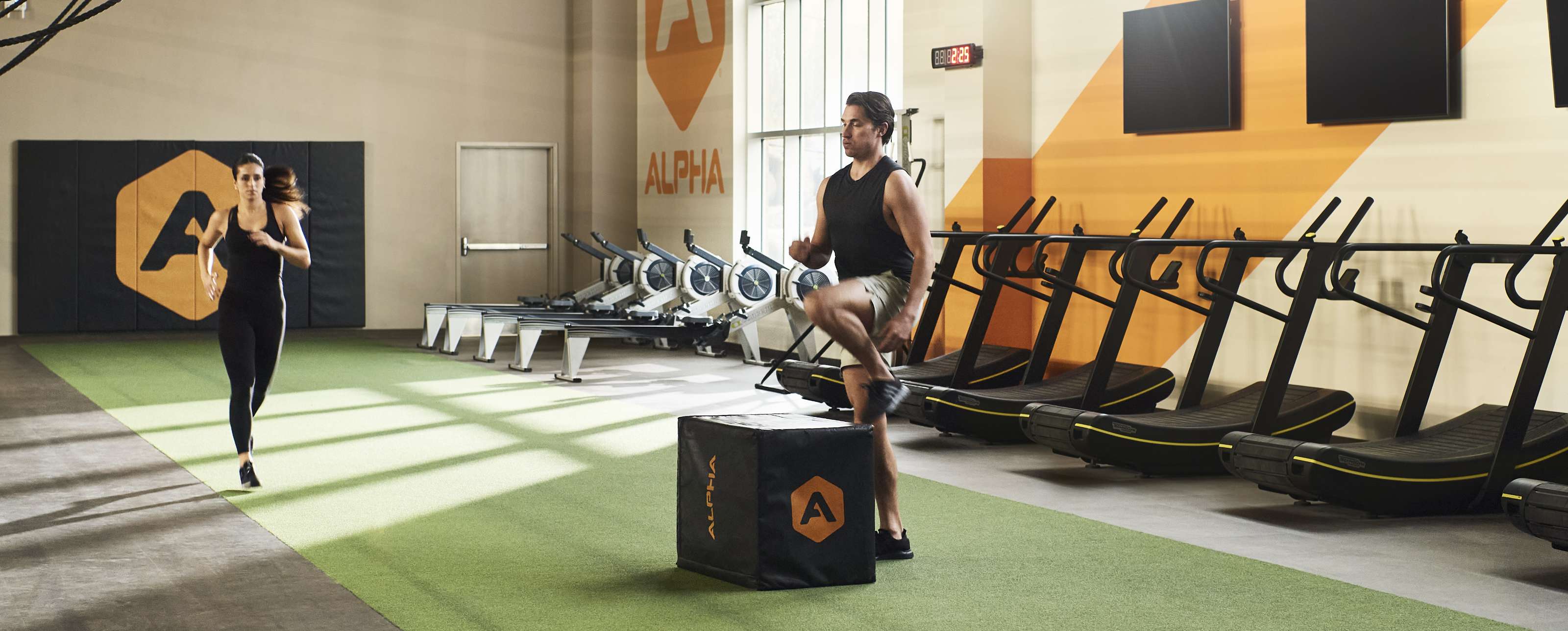 a man and a women workout in turf area surrounded by cardio machines