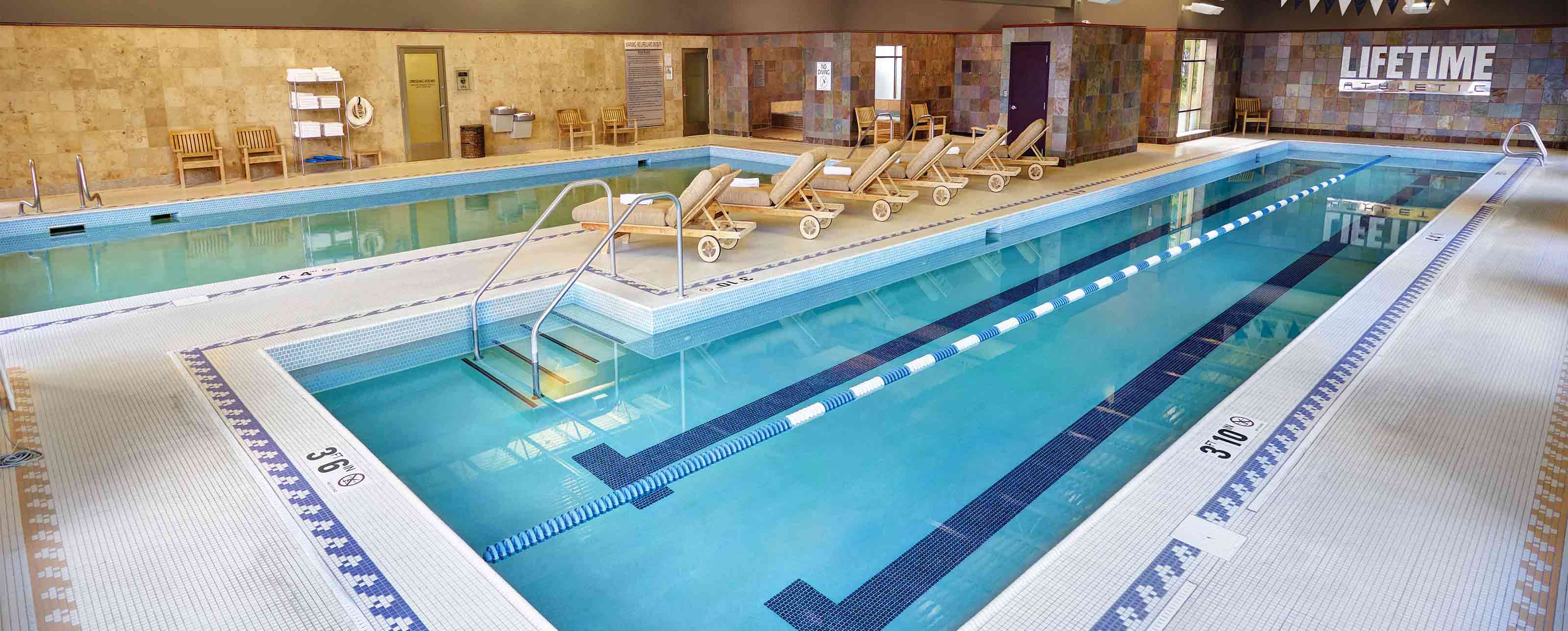 an indoor pool deck with 2 lane lap pool, lesiure pool, and lounge chairs