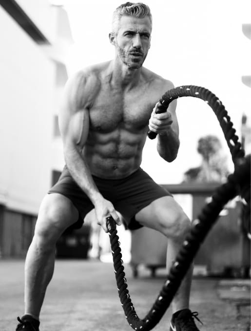 A shirt-less male doing the battle ropes.