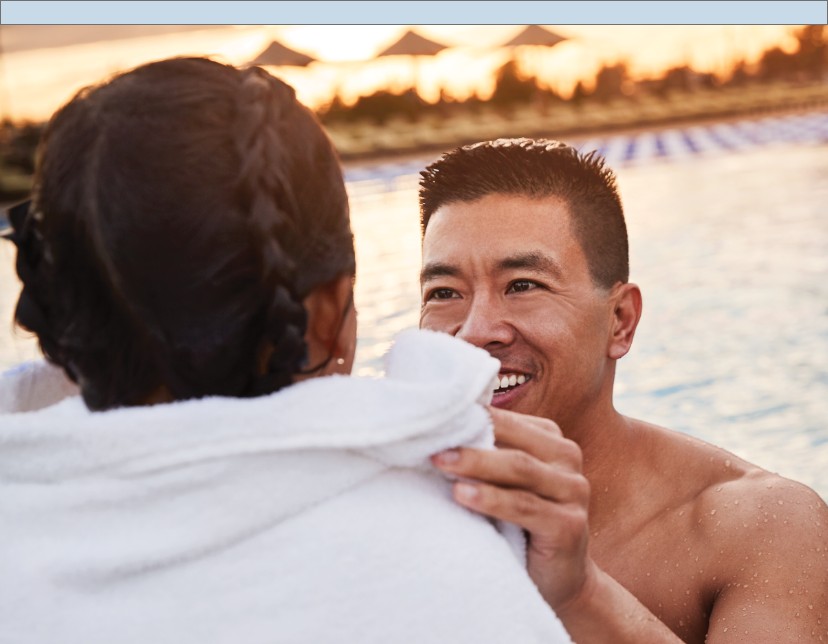 a father wraps his daughter up with a towel by an outdoor pool