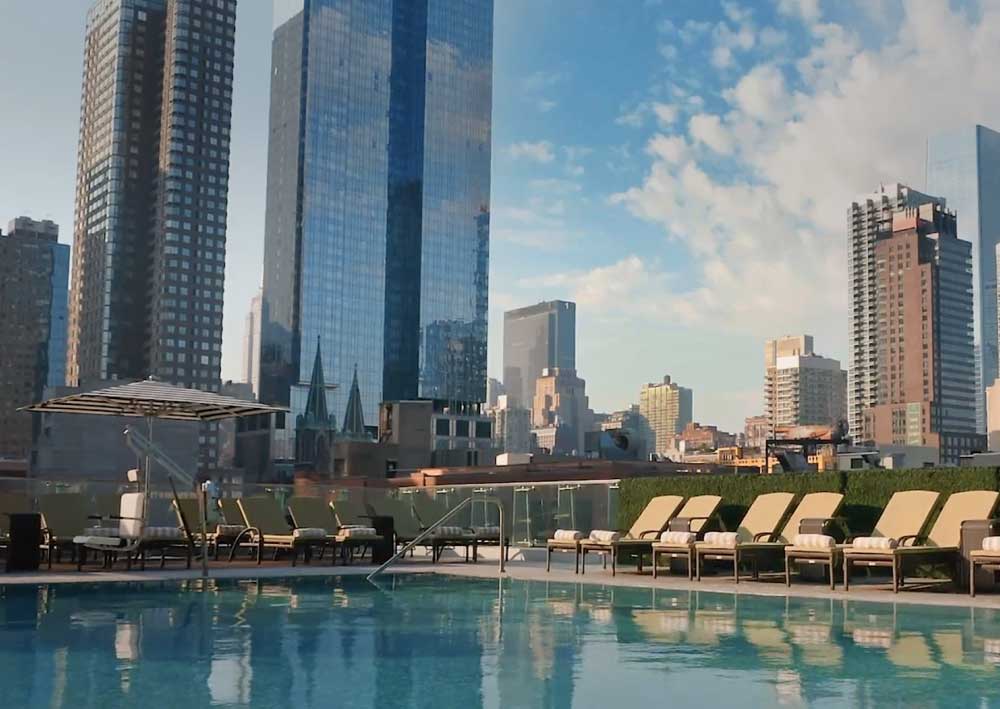 Pool lounge chairs next to a rooftop pool with skyscrappers in the background