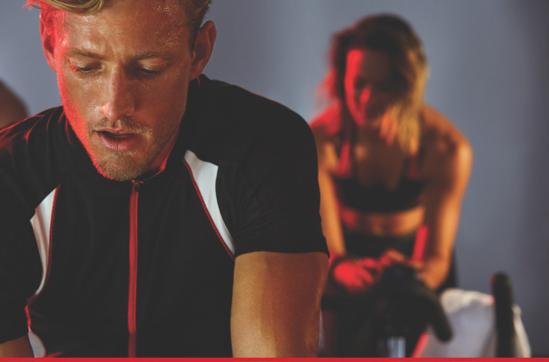 Man and woman riding stationary bikes in a cycle class