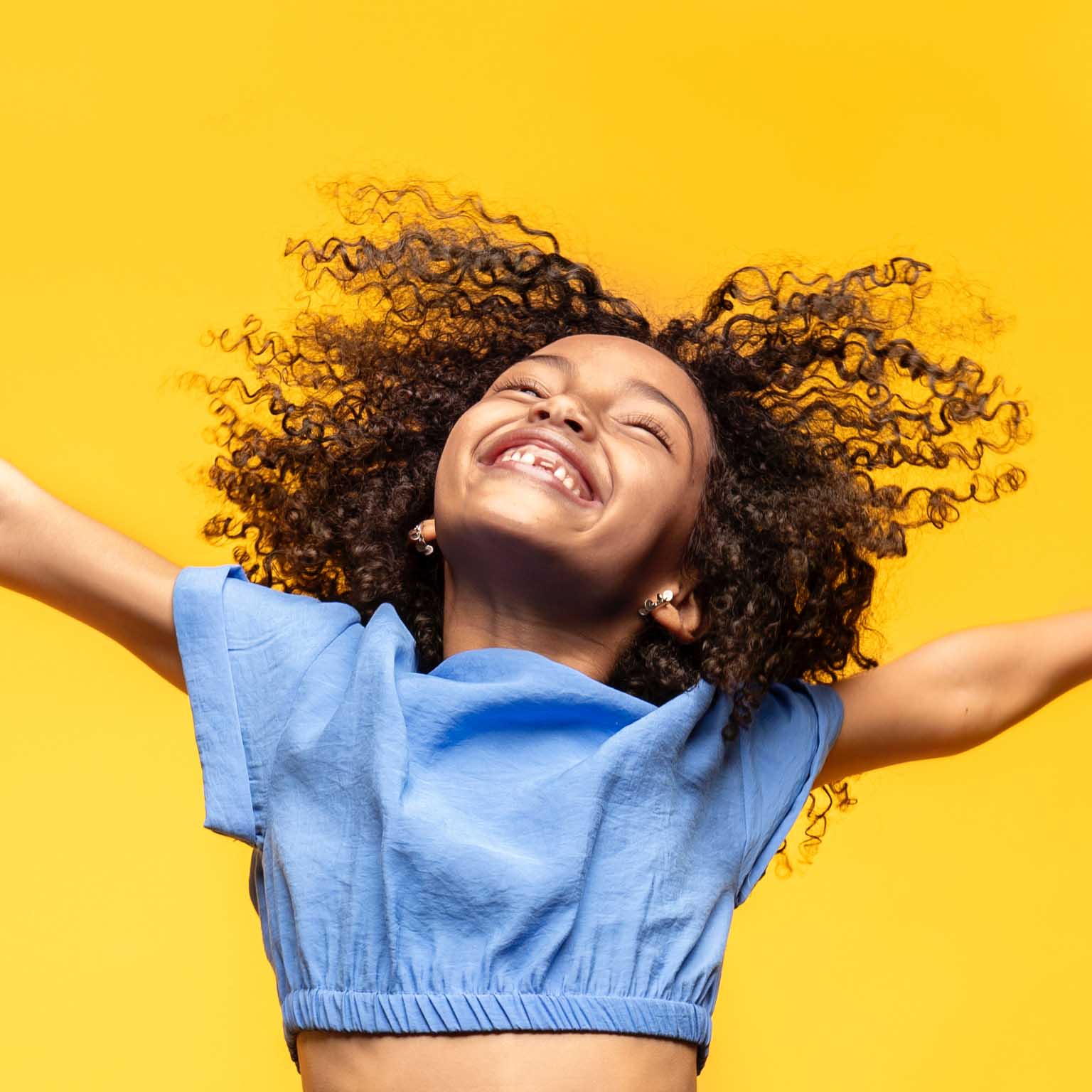 A child jumps for joy with outstretched arms and a happy smile