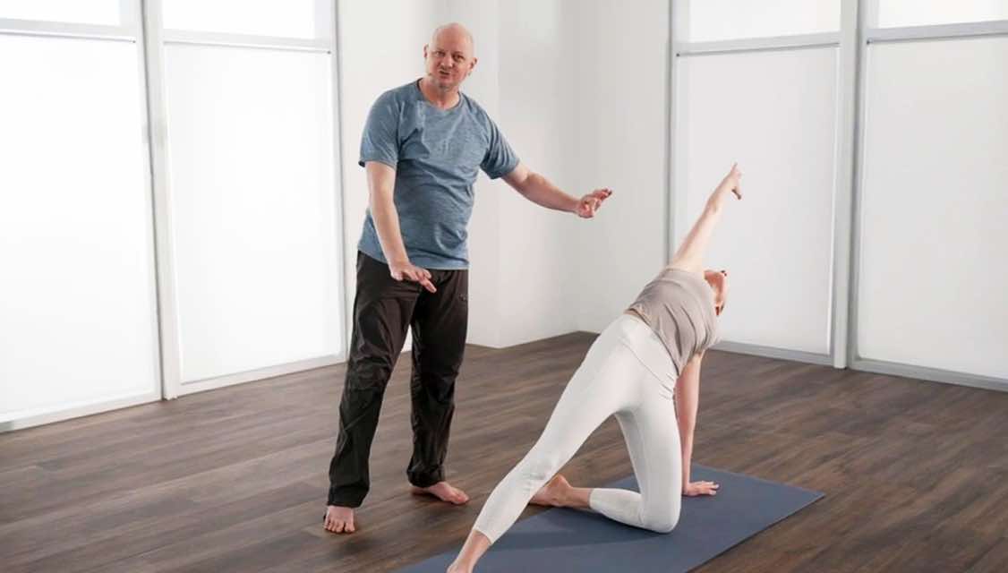 Male yoga teacher instructing woman as she does a modified back bend.