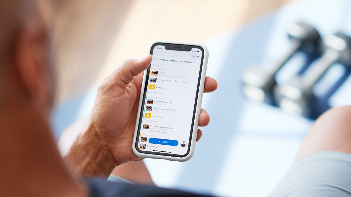 Male holding and looking at Life Time's Virtual Training App on his cell phone