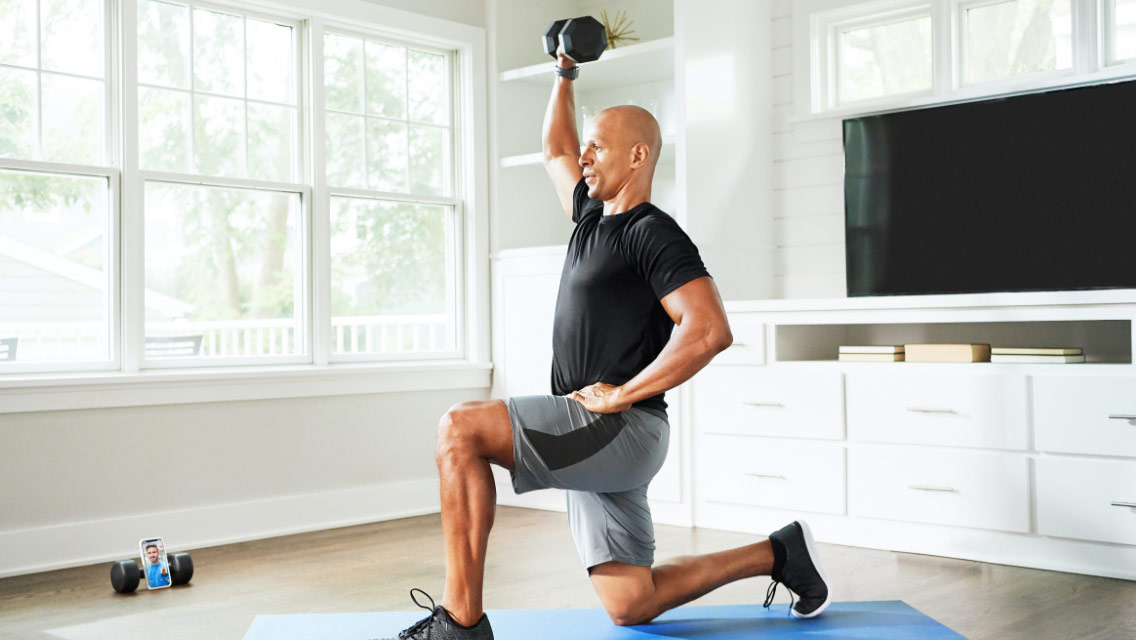 Man following directions from his trainer on his cell phone during an at-home virtual training workout session