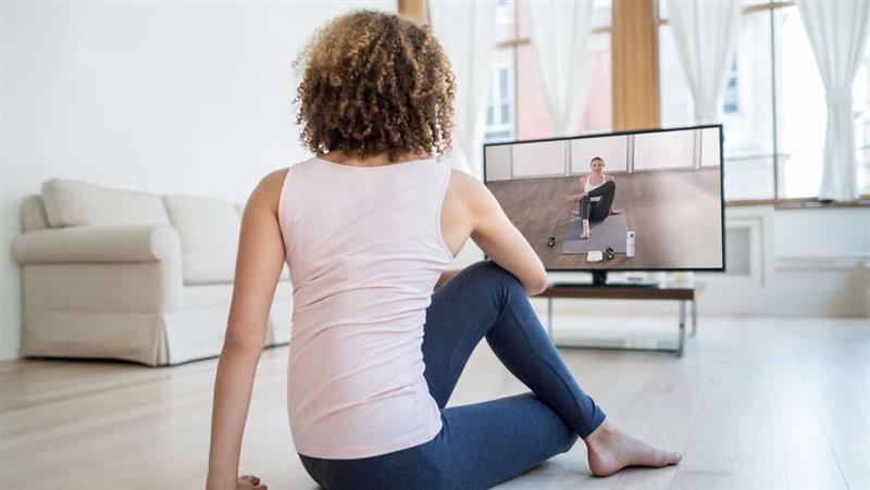 a woman mimics a stretch that is on the television in front of her