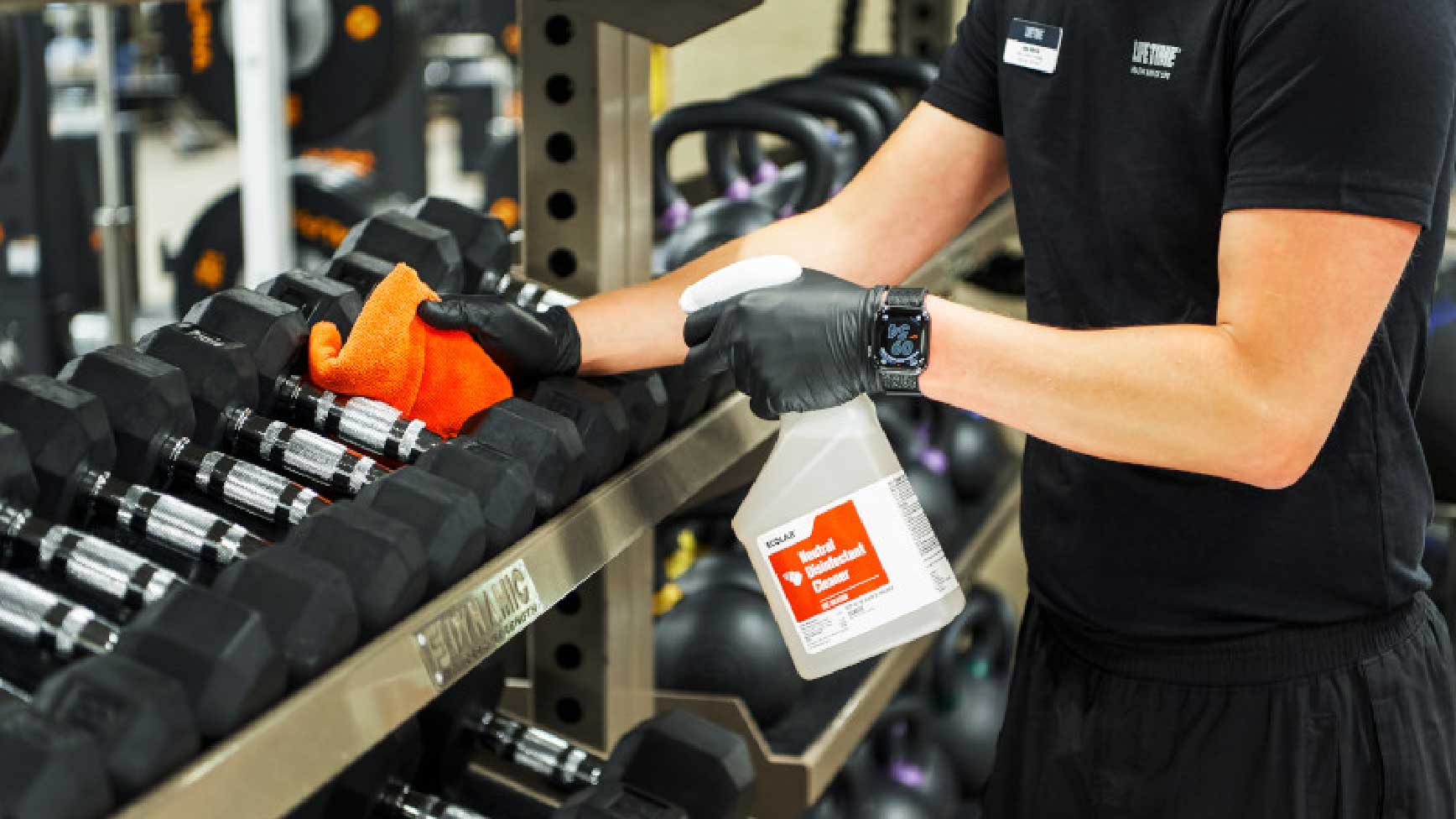 Close up shot of a team member wiping down dumbbells with virus killing disinfectant. 