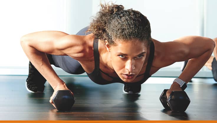 A woman in plank position with dumbbells