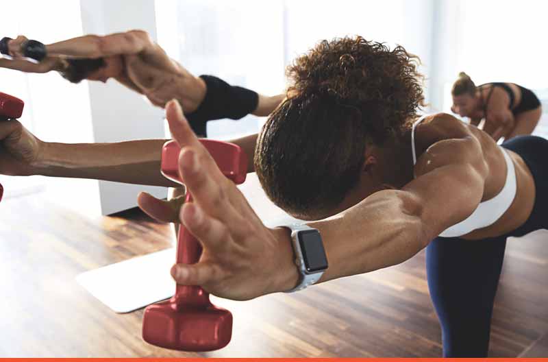 A woman and others holding a warrior yoga pose with hand weights