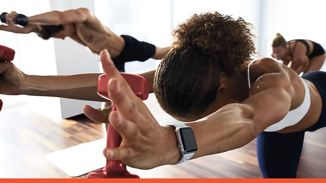 A woman and others holding a warrior yoga pose with hand weights