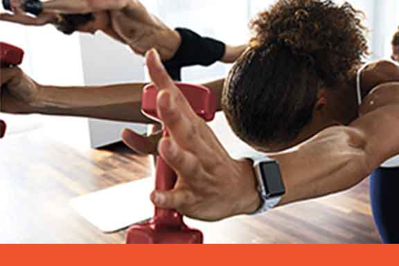 A woman and others holding a warrior yoga pose with hand weights