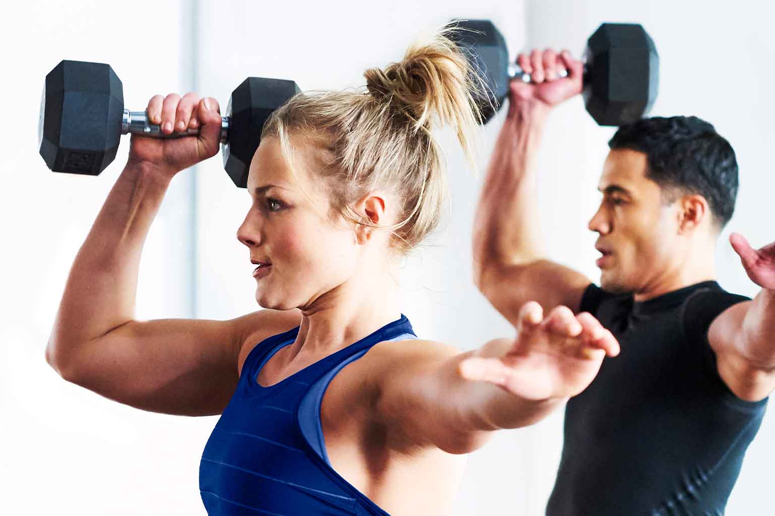 A woman in the midst of a overhead tricep extension, where her elbows are directly above her head, while she’s holding two dumbbells behind her head.